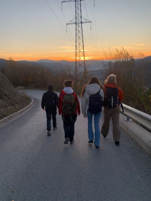 4 osebe, prostovoljke hodijo po cesti v smeri sončnega zahoda